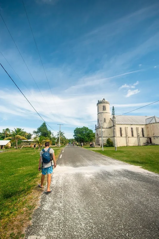 A cruise ship passenger walking towards a church on a sunny day in Lifou