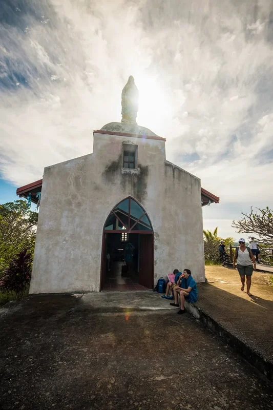 A couple cruise ship passengers sit down in front of Notre dame de Lourdes chapel in Lifou