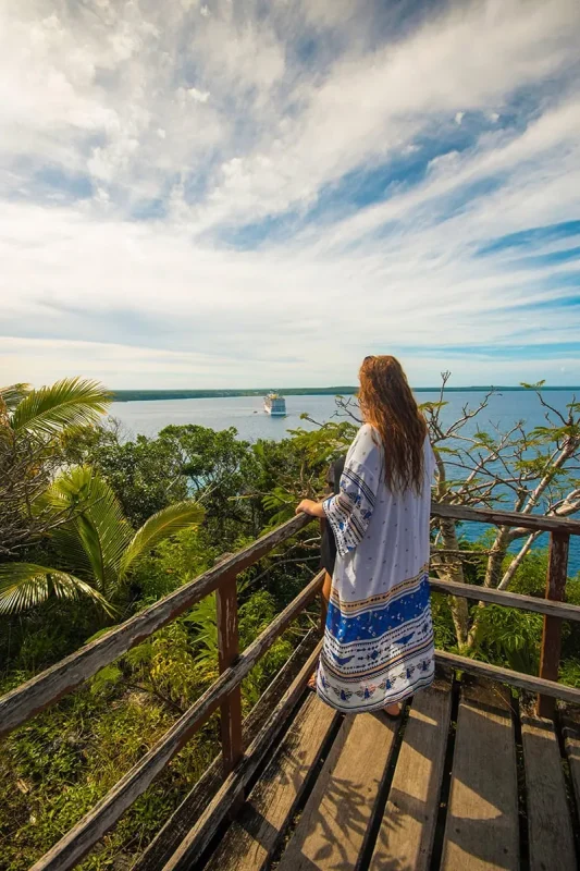 Tasha Amy standing on a wooden walkway overlooking the ocean, with a cruise ship in the distance at Lifou.