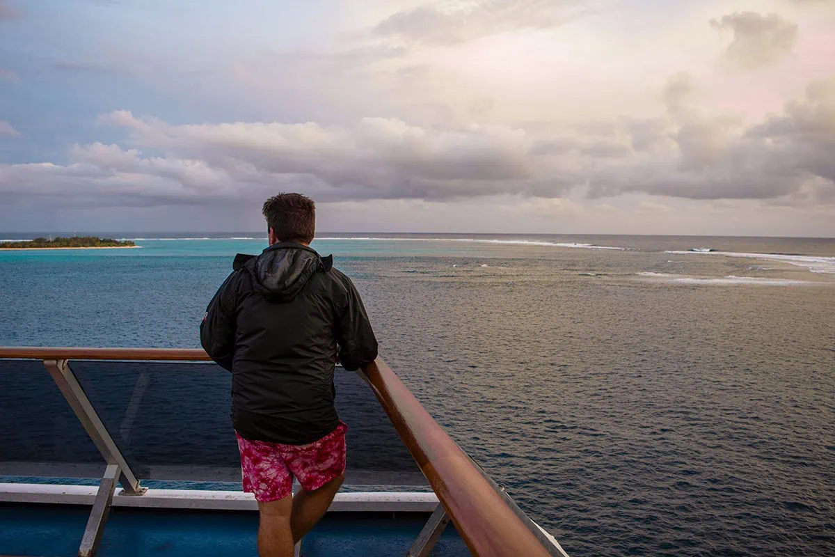 Best Things To Do On Mystery Island, Vanuatu, For Cruise Passengers 27 A man in a black jacket and red swim trunks stands on a cruise ship deck, gazing at Mystery Island at sunset