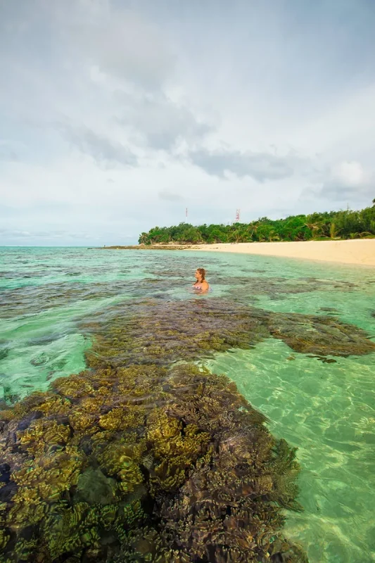 Best Things To Do On Mystery Island, Vanuatu, For Cruise Passengers 8 Tasha Amy sits in in a sandy patch on the beach at Mystery Island, surrounded by coral heads.