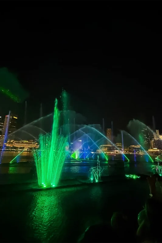 Spectra Light Show Singapore: Times, Best Views & Tips 13 Watching the Spectra Light Show at Bay front in Singapore with the fountains lit up green ueand bl