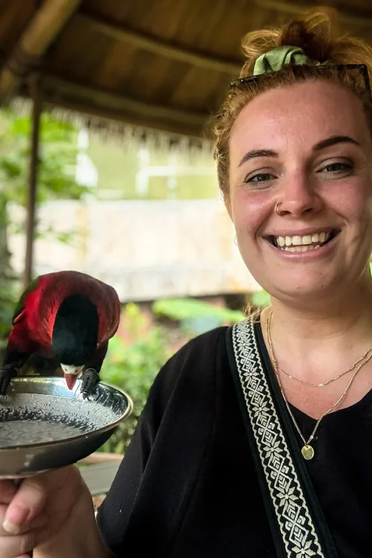 Tasha Amy holding a bowl of nectar with a Lorikeet drinking from it at Bird Paradise Singapore