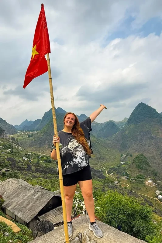 Tasha holding a Vietnamese flag at a mountain viewpoint in Ha Giang