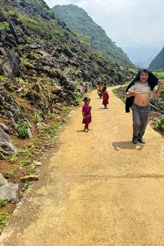 Children wearing colorful traditional clothing beside a mountain road in Ha Giang
