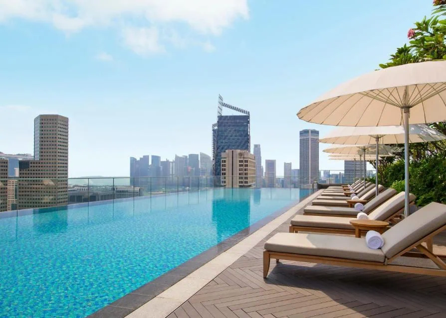 Where To Stay In Singapore: The 6 Best Areas & Hotels 35 Rooftop infinity pool and sun loungers at Andaz Singapore overlooking the city skyline.