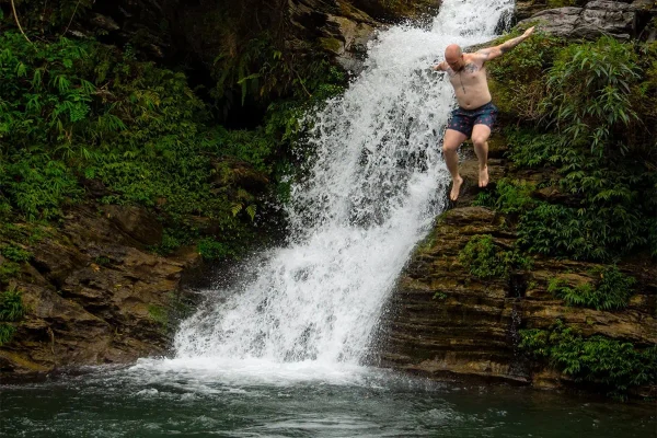 Man jumping from a rocky ledge beside Du Gia Waterfall into the natural pool below