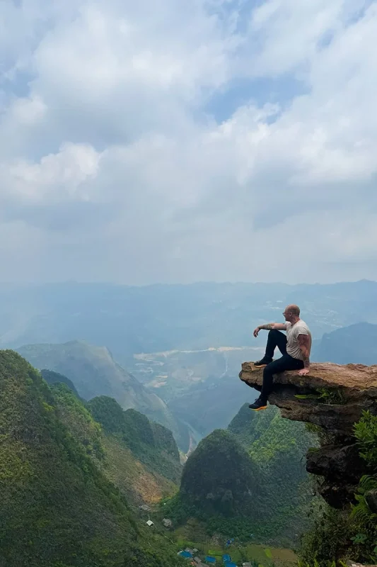 A man sitting on Death Rock overlooking the mountain valley in Ha Giang