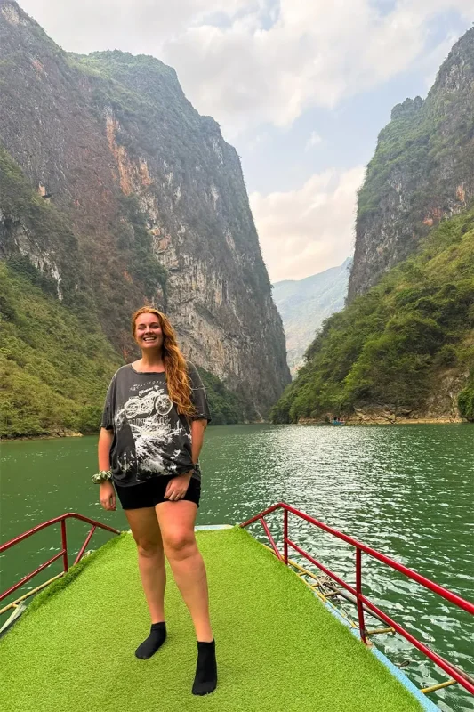 Nho Que River Boat Ride: Visiting While On The Ha Giang Loop 67 Tasha Amy standing on the front of a boat beneath the cliffs of Tu San Canyon