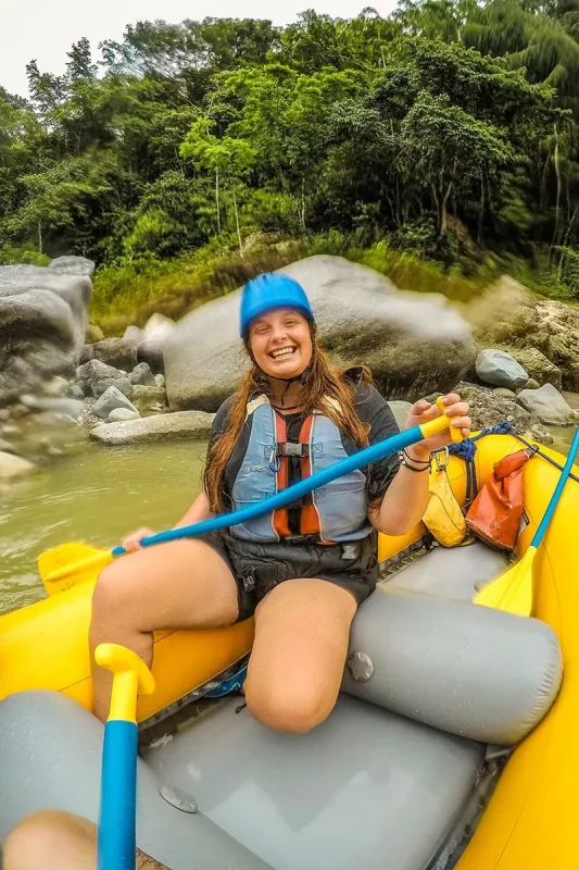 White Water Rafting In La Ceiba: My Experience On The Cangrejal River 30 Tasha Amy smiling, wearing a helmet and life jacket while sitting in a yellow raft