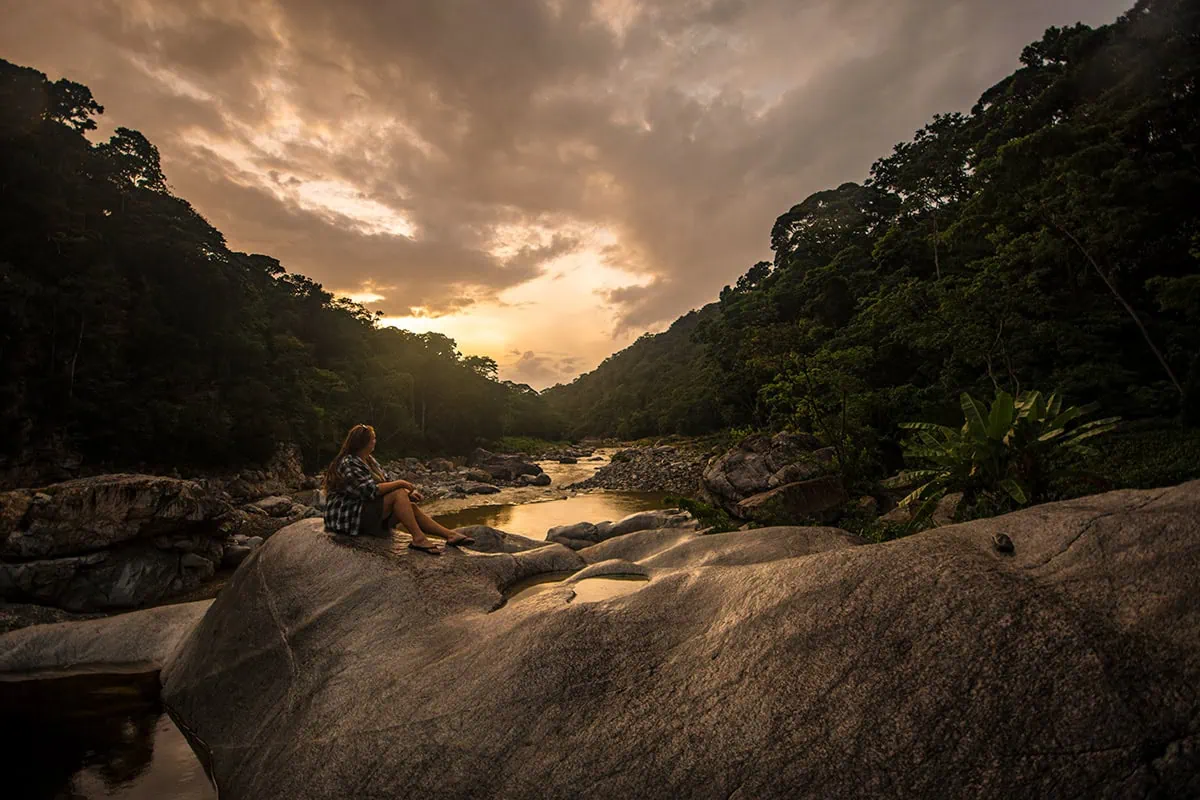 2 Weeks In Honduras Itinerary: My Recommended Route 39 Tasha Amy sitting on a large boulder beside the Cangrejal River at sunset in Pico Bonito National Park
