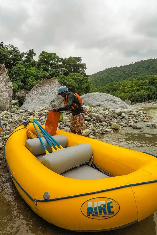 White Water Rafting In La Ceiba: My Experience On The Cangrejal River 24 Guide preparing a yellow raft and paddles beside the Cangrejal River in Pico Bonito National Park