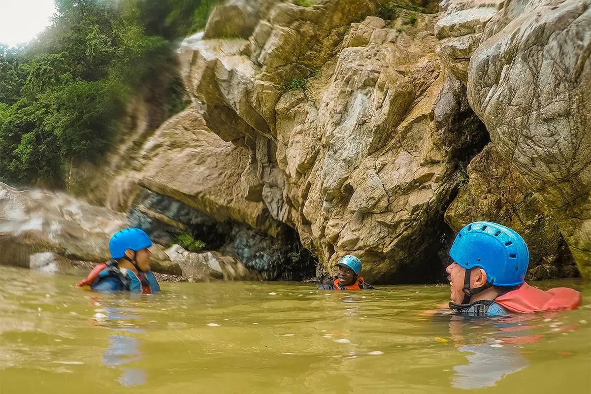 White Water Rafting In La Ceiba: My Experience On The Cangrejal River 32 Three rafters wearing helmets and life jackets swimming between rocks in the Cangrejal River