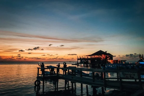 People watching the sunset from a wooden jetty beside a waterfront restaurant in Roatan, Honduras