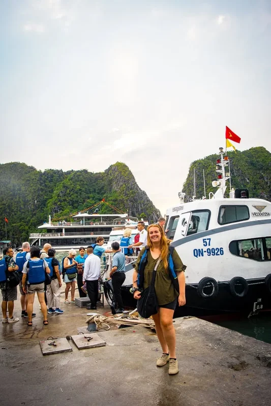 Luon Cave Ha Long Bay: Is It Worth Visiting? 63 Tasha standing on a jetty beside a transfer boat in Ha Long Bay, with passengers and limestone cliffs behind her