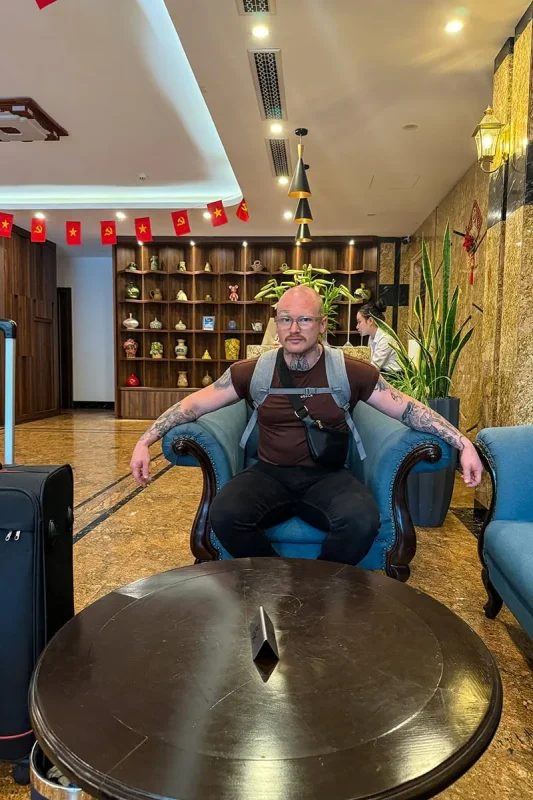 Best Hostels In Ha Giang: Where To Stay Before The Loop 66 A man sitting in a blue armchair beside luggage in the lobby of Silk River Hotel Ha Giang