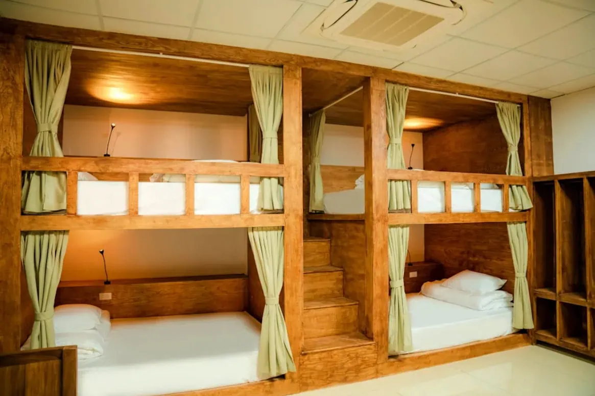 Best Hostels In Ha Giang: Where To Stay Before The Loop 59 Wooden dorm bunks at Top Of The Loop Hostel in Ha Giang with green privacy curtains, reading lights and central stairs