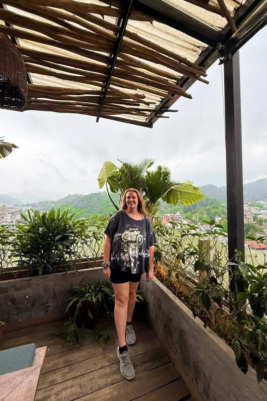 Best Hostels In Ha Giang: Where To Stay Before The Loop 58 Tasha Amy standing on the rooftop terrace at Top Of The Loop Hostel with Ha Giang City and green mountains behind
