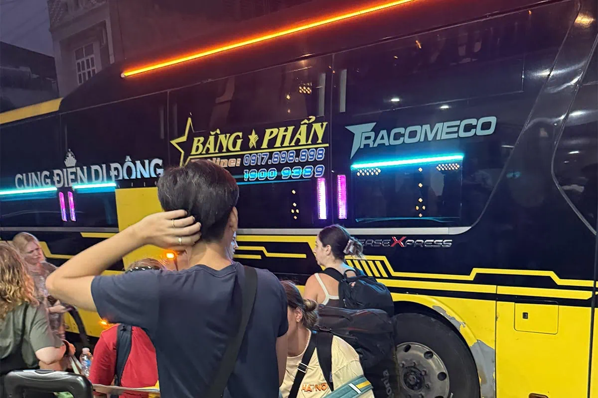 Ha Giang To Ha Long Bay: My VIP Sleeper Bus Experience (2026) 63 Backpackers with luggage standing beside a black and yellow Bang Phan sleeper bus at night.