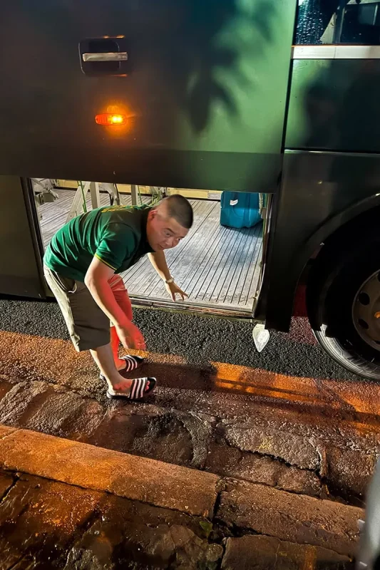 Ha Giang To Ha Long Bay: My VIP Sleeper Bus Experience (2026) 58 A man crouching beside the open luggage compartment underneath a sleeper bus at night