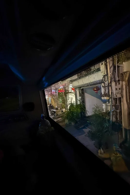 Ha Giang To Ha Long Bay: My VIP Sleeper Bus Experience (2026) 59 Shops and potted plants seen through a rain-speckled sleeper bus window at night