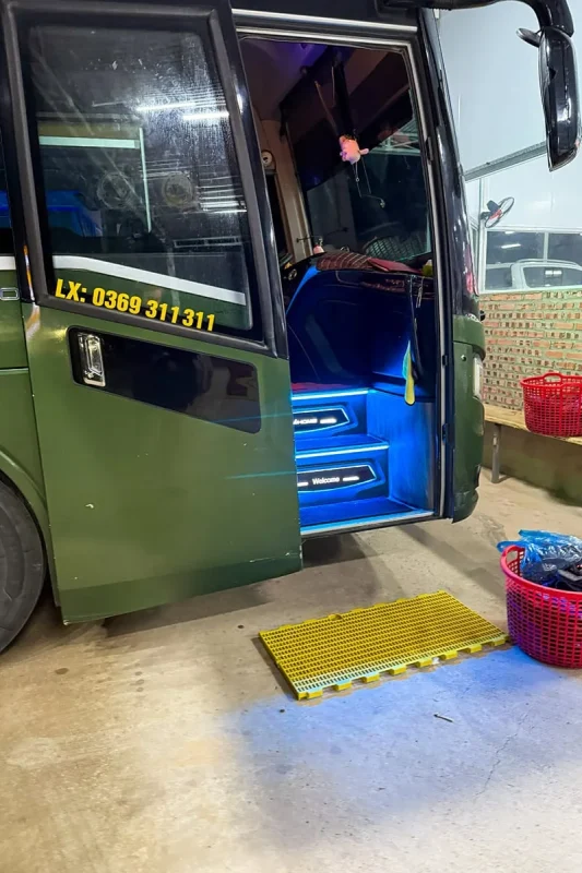 Ha Giang To Ha Long Bay: My VIP Sleeper Bus Experience (2026) 66 Open sleeper bus entrance with blue-lit steps and baskets of slippers beside the door