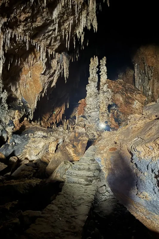 An uneven stone path winding past stalactites and tall rock formations inside Ta Lung Cave