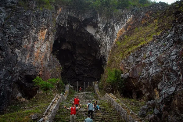 Visitors on the stone staircase below the enormous entrance to Ta Lung Cave in Ha Giang